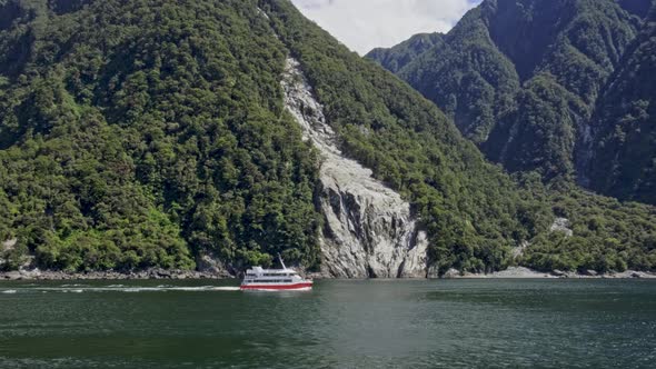 Tourist Boat Cruising At Milford Sound With Scenic Mountains In The Background At Fiordland, New Zea