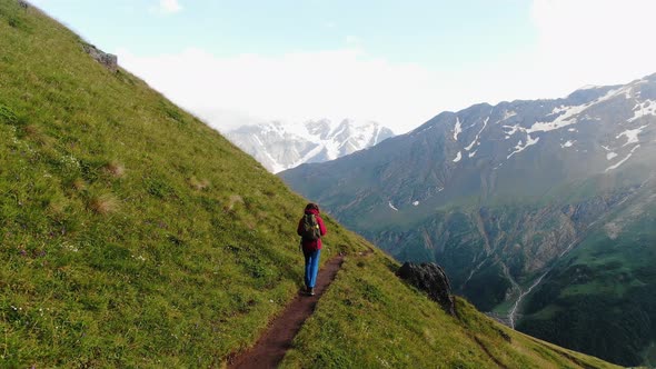 Lady with Backpack Walks on Hillside Path with Grass Carpet