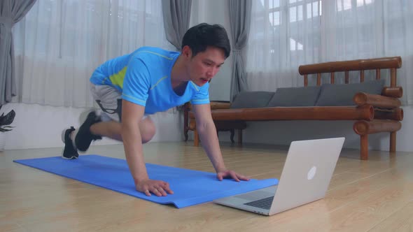 Man Doing Mountain Climber Exercises While Watching Online Tutorial On Laptop At Home