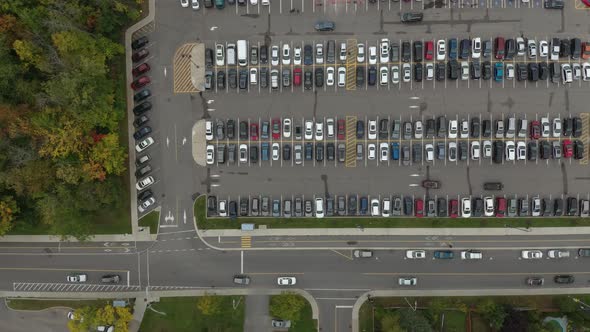 Vertical overhead drone shot of busy parking lot with cars driving within it