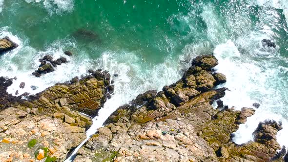 Turquoise water meeting a rocky coastline on an island landscape, rising drone view.