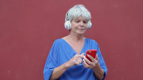 Senior woman using mobile smartphone listening and dancing to music playlist outdoor