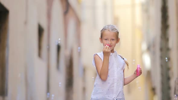 Adorable Little Girl Outdoors Blowing Soap Bubbles in European City. Portrait of Caucasian Kid Enjoy