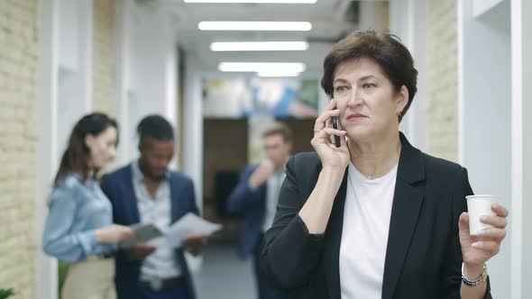 Beautiful Mid-adult Caucasian Woman with Coffee Cup Talking on the Phone with Blurred Multiracial