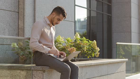 Hispanic Businessman Sitting Outside with Laptop Working Remote Distant Job Outdoors Near Office