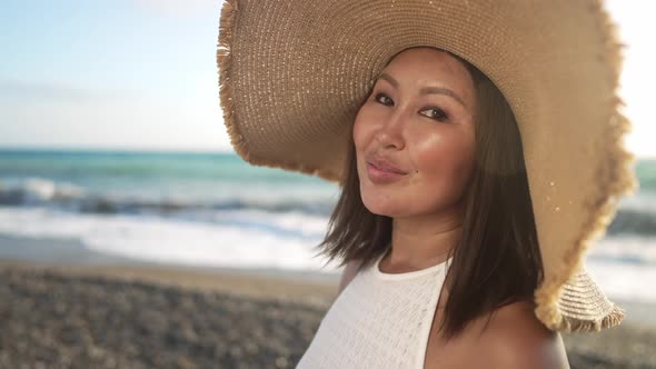 Gorgeous Asian Middle Aged Woman in Straw Hat Posing on Mediterranean Sea Beach in Slow Motion