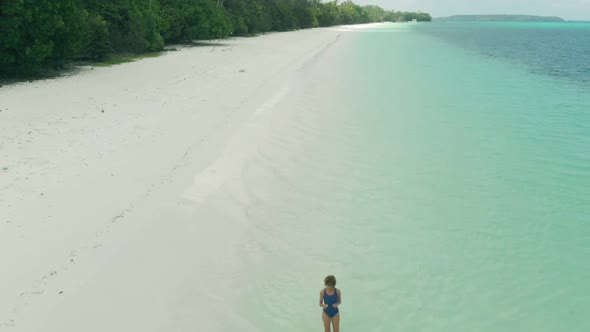 Aerial: Woman walking on white sand beach turquoise water tropical coastline Pas