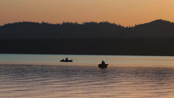 A Silhouette of People Sitting in a Boat and Fishing on Nature While the Sunset