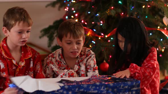 Three kids open Christmas gift together alt