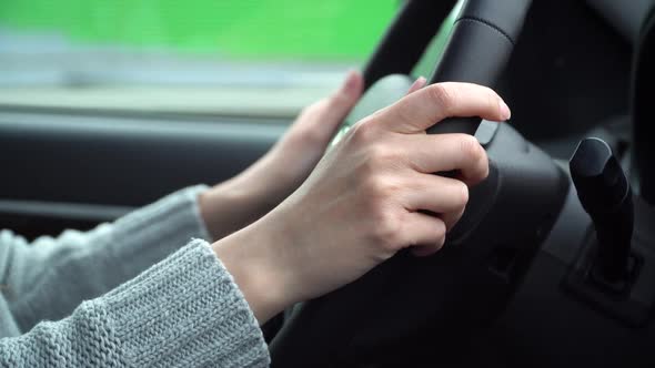 Hands of a young woman holding the steering wheel of a car while driving