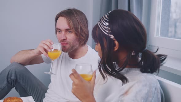 Young Multiracial Couple Drinking Orange Juice and Having Conversation in the Bed