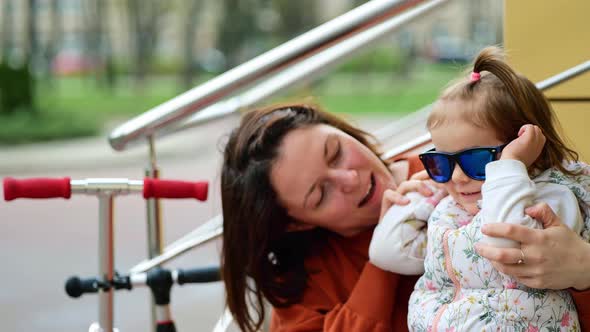 Happy Mother and Little Daughter Getting Fun and Trying On Sunglasses