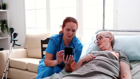 Female Nurse Helping Old Woman To Use Smartphone