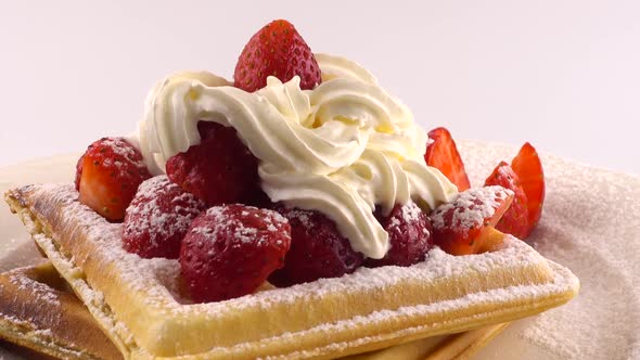 Belgian waffles with strawberry, whipped cream and powdered sugar on a plate