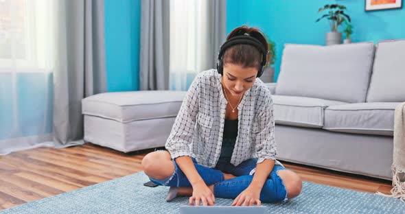 Ambitious Girl Sits on the Floor Carpeted in the Living Room with a Laptop