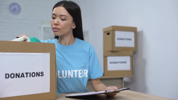 Young Volunteer Checking Clothes Donation Box and Making Notes, Humanitarian Aid