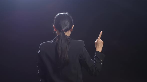 Back View Of Asian Speaker Woman In Business Suit Showing Index Fingers Up While Speaking On Stage