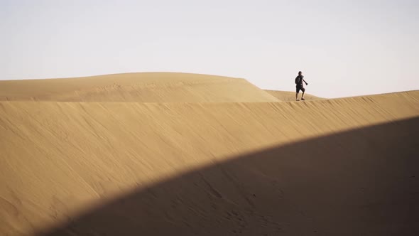 Man Walking Along Sand Dune In Desert
