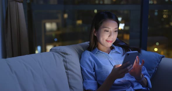 Woman use of mobile phone and sit on sofa at night