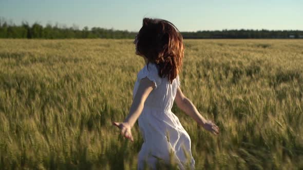A Young Woman Runs Across the Field in a White Dress. Happy Girl in a Green Wheat Field. Slow Motion