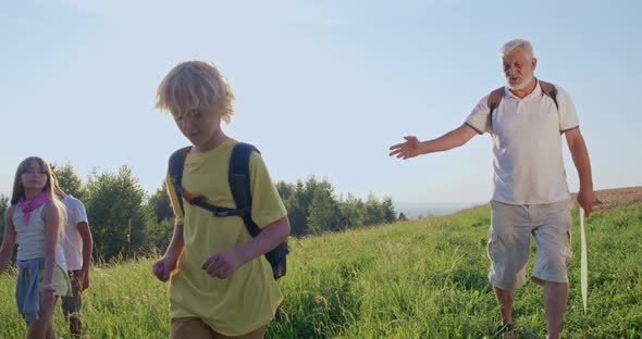 Middleaged Man with Teens Walking Down Green Hill in Summer