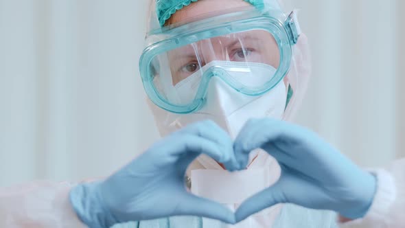 Close Up of a Doctor in a Protective Medical Suit Shows a Heart Folded From His Hands.