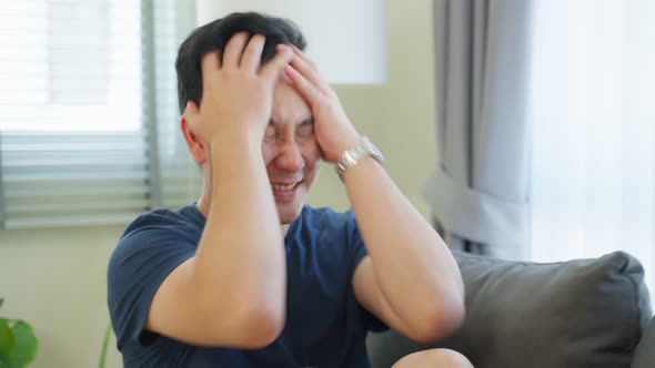 Portrait of Asian young angry man sitting alone on sofa in living room.