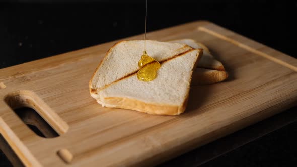 Honey flowing in slow motion on two toasted bread on a cutting board.