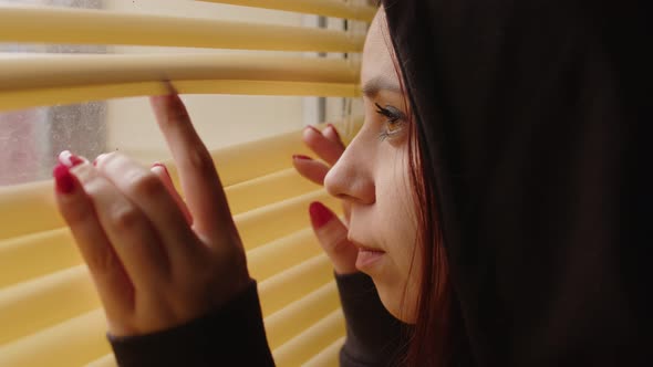 Close Up of Young Woman Watching Through Window Blinds at Home