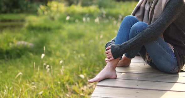 Woman sitting on the wooden walking path and swing the legs