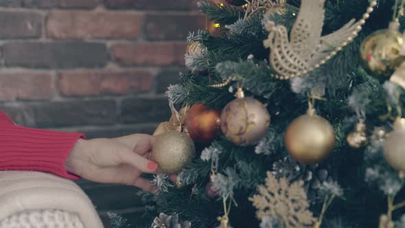 Young Woman Touches Golden Ball and Bow on Christmas Tree