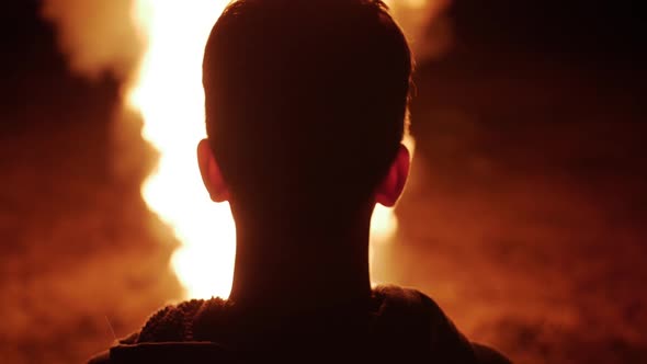 Silhouette Of Teen Boy Watching Large Flames of Fire Burn In Slow Motion