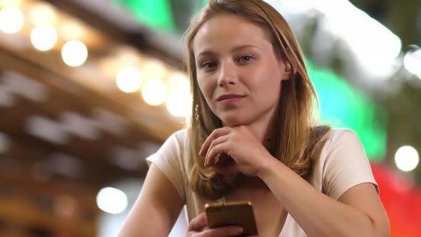 Tense Teenage Girl Looking at Camera Holding a Phone in Her Hand.