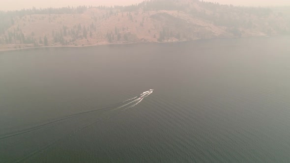 Aerial Above Eastern Washington Lake With Boat Towing Inner Tubes In Wildfire Smoke alt