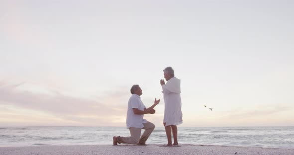 Hispanic senior man proposing to senior woman on beach at sunset