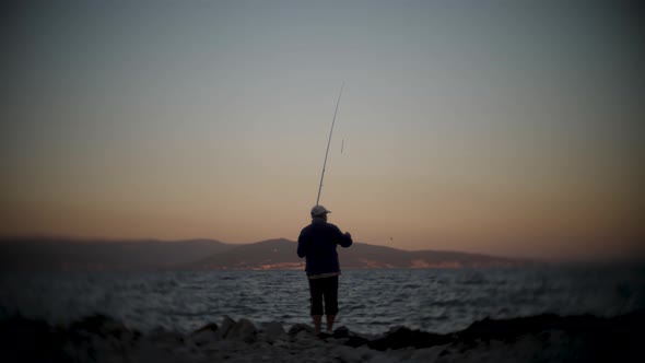 One Man a Fisherman Stands on the Beach at Sunset and Catches Fish