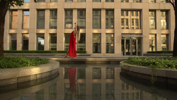 Beautiful Young Girl Dancing on the Street of a Modern City and Is Reflected in the Water