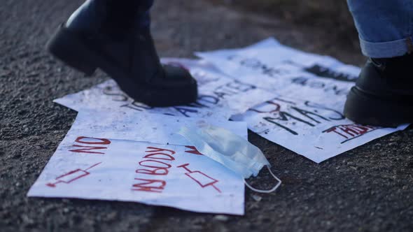 Female Feet in Shoes Passing Antivax Placards and Coronavirus Face Mask on Ground Outdoors