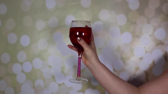A woman's hand holding a glass of rose wine on a glittery background