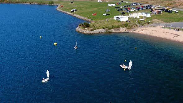 people practicing in the sailing school of the lake with beach, parking full of cars. Tiro de drone