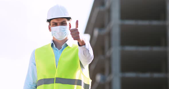 Professional Builder in Protective Mask and Helmet Gesturing Thumb Up, Standing at Construction Site