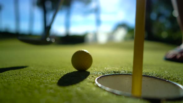 Mini Golf Yellow Ball with a Bat near the Hole at Sunset