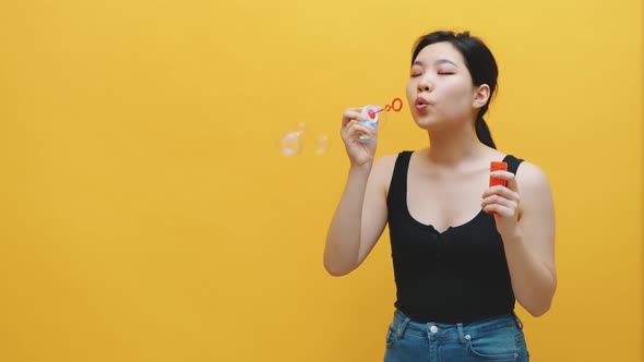 Happy Young Asian Woman Blowing Soap Bubbles. Isolated on Yellow Background. Slow Motion