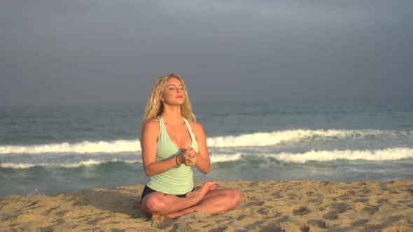 A young woman doing yoga on the beach while sitting.