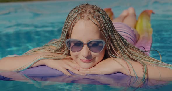 Happy Girl with Afro Pigtails Swims on an Inflatable Mattress in the Pool Resting and Enjoying the
