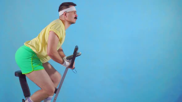 Funny Young Man From the 80's with a Mustache and Glasses on Exercise Bike on a Blue Background