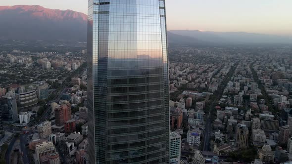 Aerial orbit of curtain wall Costanera Center skyscraper, Mapocho river, hills in background at blue