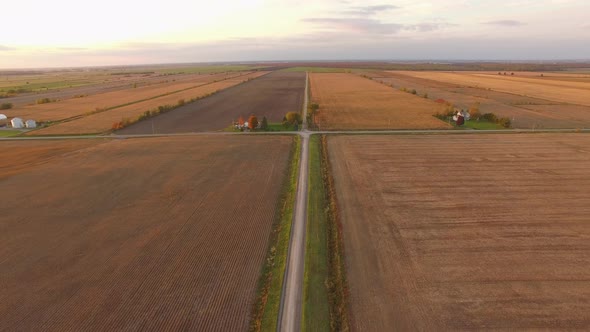 Aerial view of flat open farmland with freshly plowed fields and plots ready for harvest. A long str
