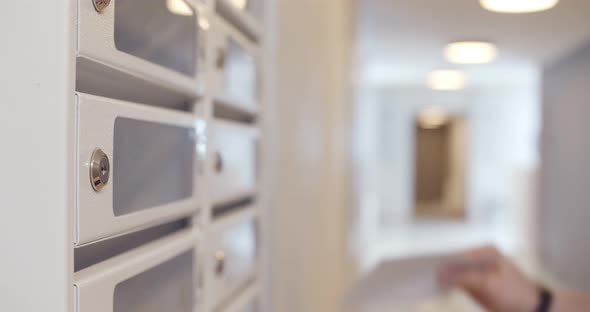 Close Up of Postman Putting Letters in Mailbox in Apartment House Lobby