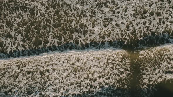 Top down view of tropical beach, foamy ocean waves washing sand. Waves hitting sand beach